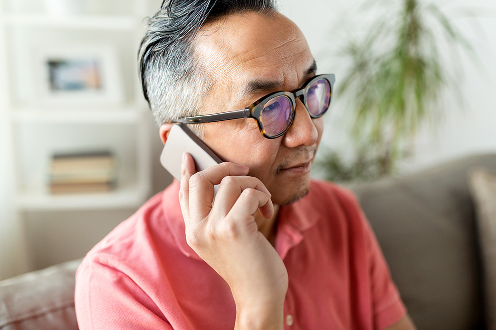 technology, people, lifestyle and communication concept - close up of asian man sitting on sofa calling on smartphone at home